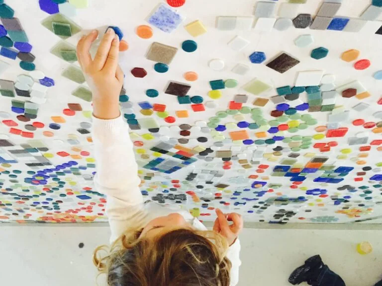 Des mains composent avec de petites pièces colorées sur une surface transparente